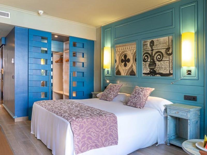 Chambre d'hôtel avec un grand lit, des panneaux muraux bleu-vert et des œuvres décoratives au-dessus du lit