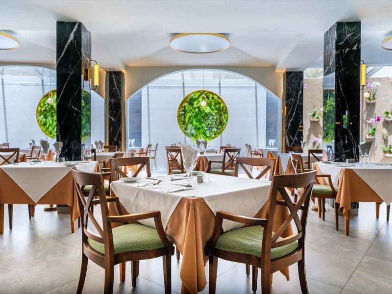 Intérieur de restaurant élégant avec tables rondes et carrées dressées pour le dîner sous des luminaires modernes.