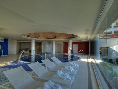 Innenraum mit Whirlpool, weißen Liegestühlen, großen Fenstern und hellem Tageslicht.