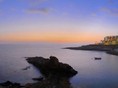 Panorama einer ruhigen Küstenlandschaft mit Felsen, klarem Wasser und hellem Himmel bei Sonnenuntergang.