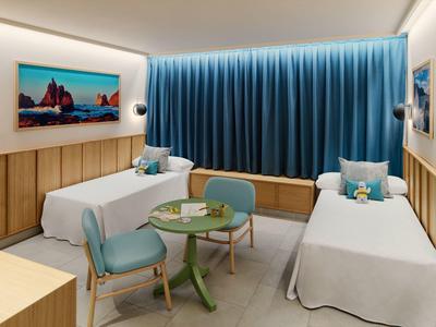 Zwei Einzelbetten, runde grüne Tischchen, blaue Stühle und lange blaue Vorhänge in hellem Zimmer.