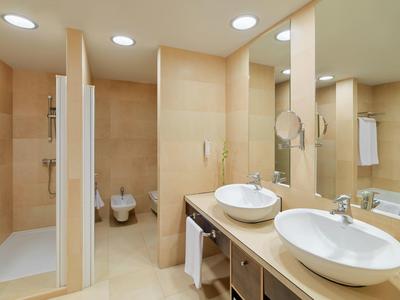 Modernes Badezimmer mit zwei runden Waschbecken, großer Spiegel, Dusche, Bidet und hellen Fliesen.