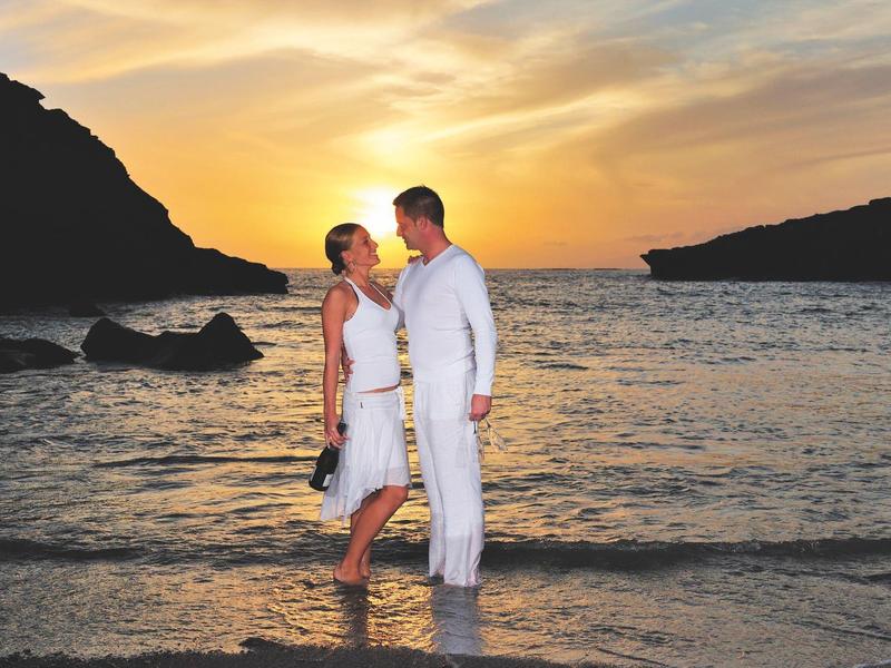 Ein Paar steht im flachen Wasser bei Sonnenuntergang zwischen zwei Hügeln am ruhigen Strand.