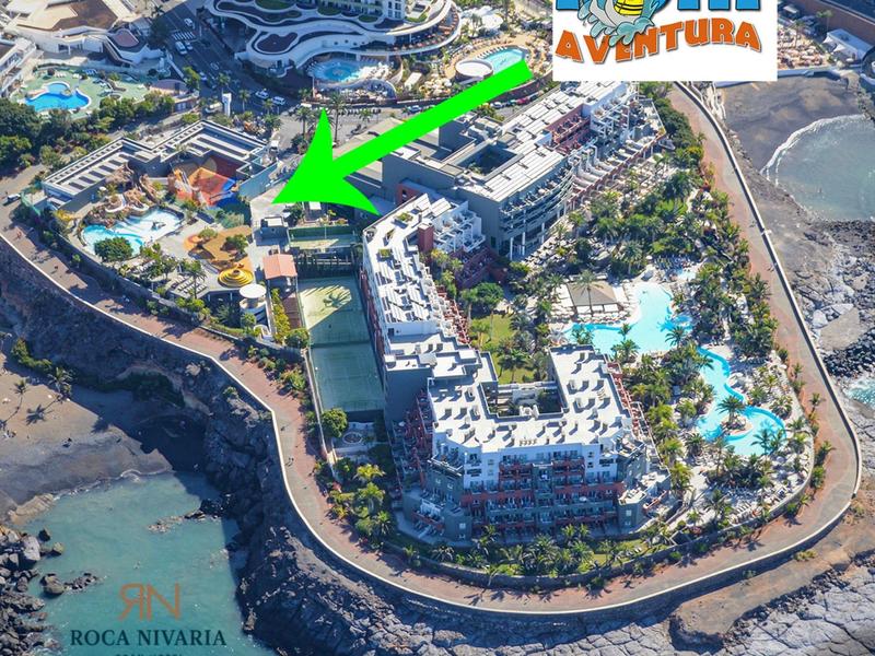 Luftaufnahme eines Küstenresorts mit Pool, Strand und mehrstöckigen Gebäuden unter Sonnenschein.