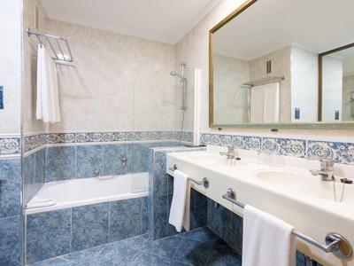 Moderner Badezimmerspiegel über weißem Waschbecken, blaue und weiße Fliesen, Badewanne mit Duschvorhang.