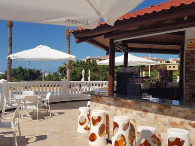 Dachterrasse mit weißen Tischen und Stühlen, Sonnenschirmen, Barbereich und blauem Himmel.