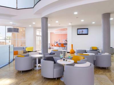 Moderne Hotellounge mit grauen Sesseln, orangefarbenen Akzenten und hellen Holzböden.