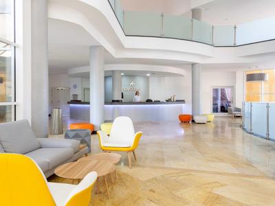 Großer heller Empfangsbereich mit moderner Möblierung in Weiß und Gelb, Glastrennwänden und Marmorboden.