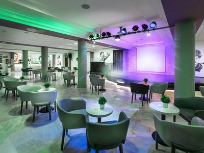 Moderner Veranstaltungsraum mit runden Tischen, Stühlen und einer kleinen Bühne mit Lichteffekten.