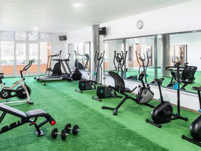 Moderner Fitnessraum mit Trainingsgeräten und grüner Teppichfläche