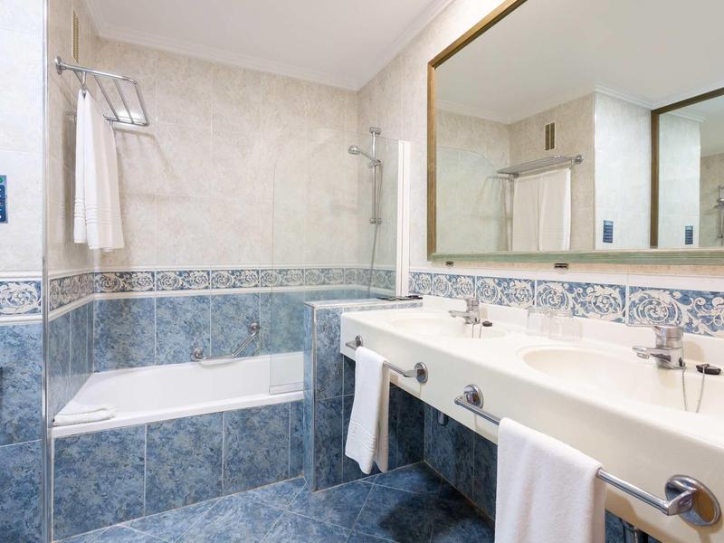 Moderner Badezimmerspiegel über weißem Waschbecken, blaue und weiße Fliesen, Badewanne mit Duschvorhang.