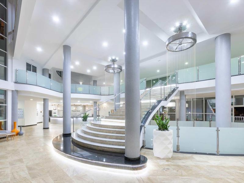 Helle, moderne Eingangshalle mit großer Treppe, Glasgeländern und runden Säulen.