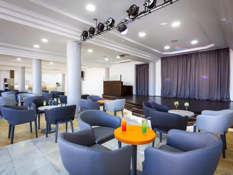 Moderner Konferenzraum mit blauen Sesseln, runden Tischen und Bühne mit Vorhang im Hintergrund.