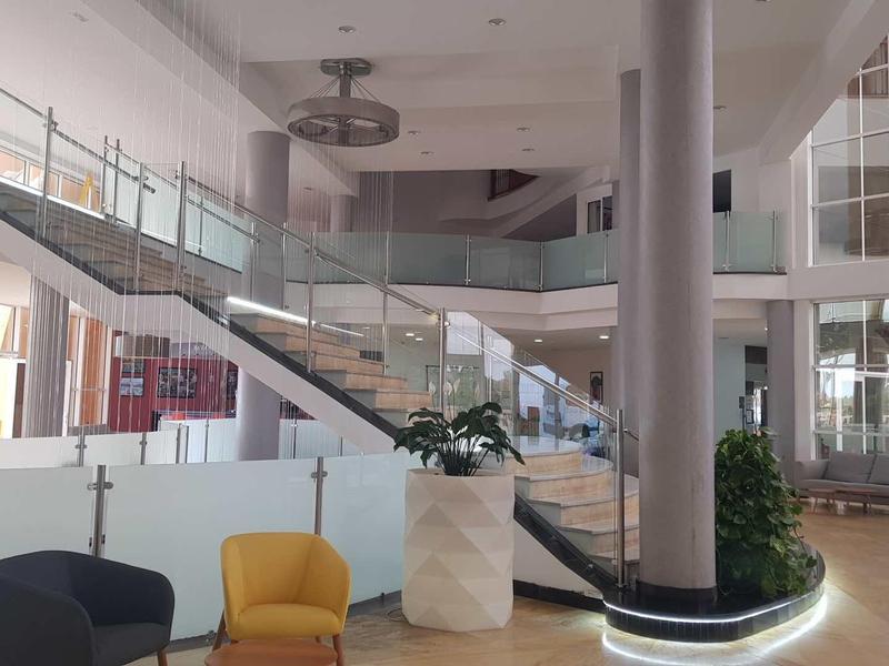 Moderne Empfangshalle mit Treppe, großen Fenstern, Pflanzen und farbigen Sesseln.