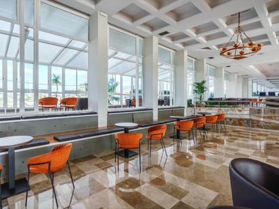 Sala luminosa con grandi finestre, sedie arancioni e pavimento in marmo lucido.