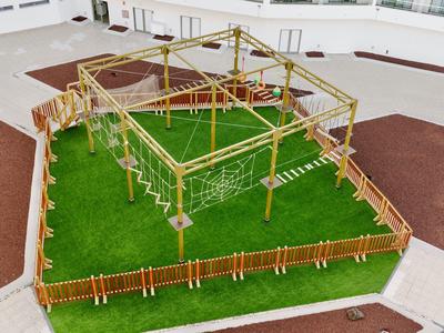 Percorso avventura in legno con reti e corde su prato verde recintato.