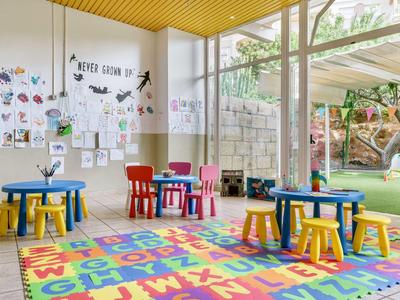 Angolo colorato per bambini con sedie, tavoli e tappeto alfabetico in una stanza luminosa.