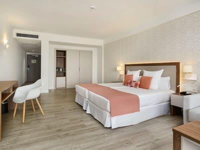 Camera d'hotel moderna con letto matrimoniale, scrivania, sedie bianche e arredi minimalisti.