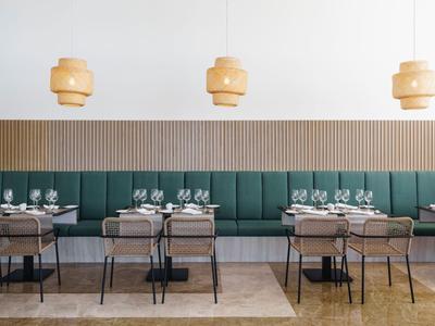 Moderne eetruimte met groene gestoffeerde zitplaatsen, houten tafels en hangende houten lampen.