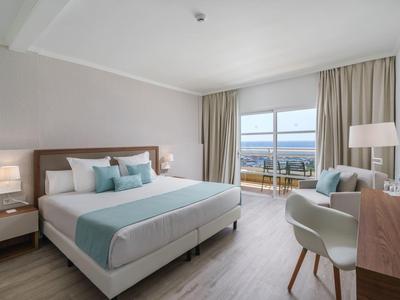 Camera d'hotel luminosa con letto matrimoniale, balcone con vista mare, arredi moderni.