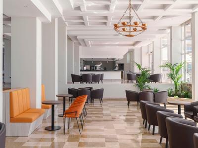 Interno moderno di un bar con vari posti a sedere e grandi finestre luminose.