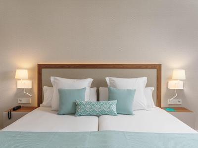 Letto matrimoniale bianco con cuscini azzurri in una stanza d'hotel moderna e luminosa.