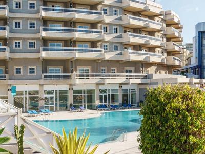 Hotel moderno con piscina all'aperto e balconi, cielo azzurro chiaro.