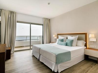 Camera d'hotel luminosa con letto matrimoniale, balcone e arredo moderno.