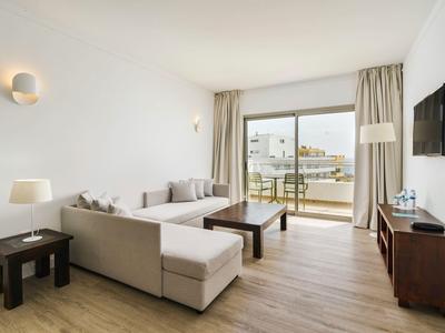 Soggiorno luminoso con divano, tavolino, TV a parete e balcone con vista città.