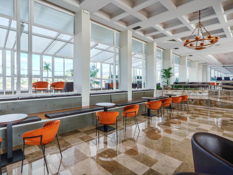 Sala luminosa con grandi finestre, sedie arancioni e pavimento in marmo lucido.