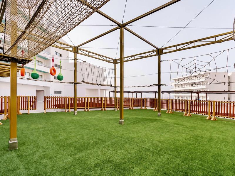 Area giochi esterna con strutture per arrampicata su prato artificiale.