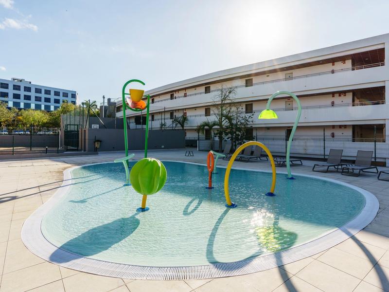 Piscina per bambini con giochi d'acqua colorati in un cortile soleggiato dell'hotel.