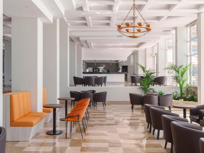 Interno moderno di un bar con vari posti a sedere e grandi finestre luminose.