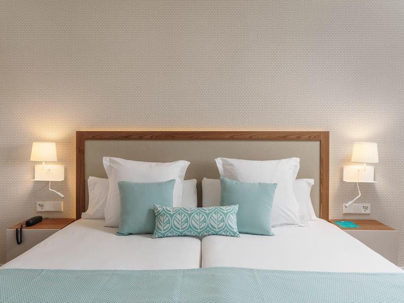 Letto matrimoniale bianco con cuscini azzurri in una stanza d'hotel moderna e luminosa.