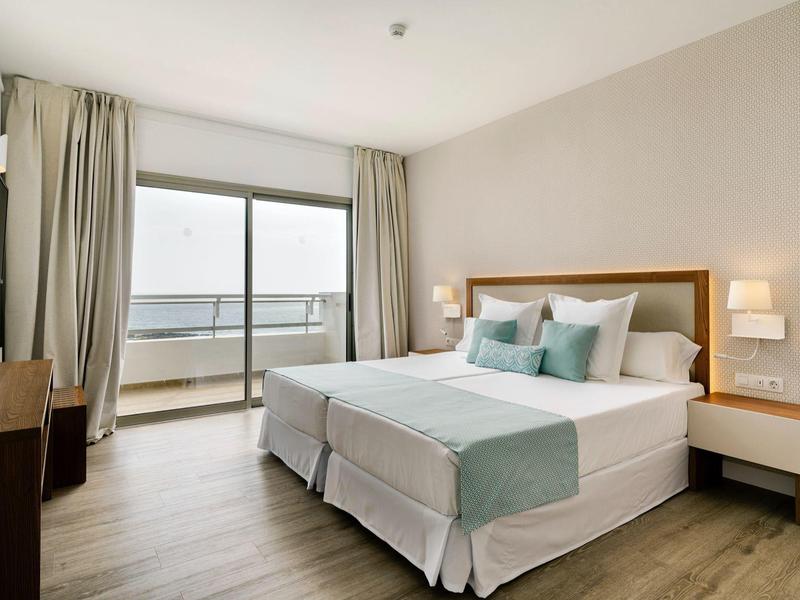 Camera d'hotel luminosa con letto matrimoniale, balcone e arredo moderno.