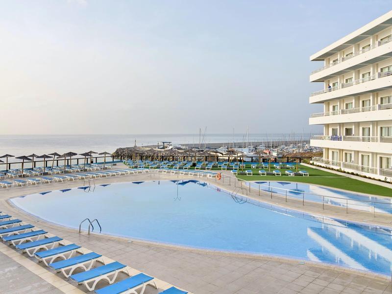 Piscina esterna vicino al mare con lettini e ombrelloni in un hotel moderno.