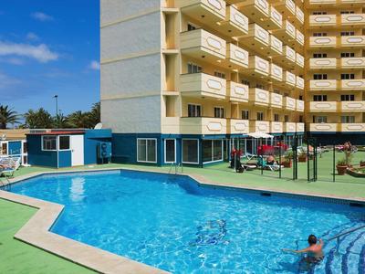 Außenbereich mit blauem Swimmingpool, Spielplatz, mehrstöckigem Gebäude und blauem Himmel.