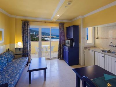 Salon lumineux avec coin cuisine, canapé, table et balcon avec vue sur la montagne.