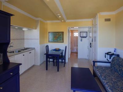 Coin chambre d'hôtel confortable avec cuisine, table à manger et canapé en tons clairs.