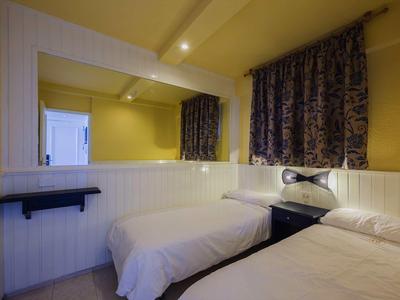 Petite chambre d'hôtel avec deux lits simples, murs jaunes et grand miroir.