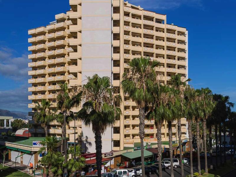 Nowoczesny żółty budynek hotelu z balkonami i palmami na pierwszym planie pod niebieskim niebem