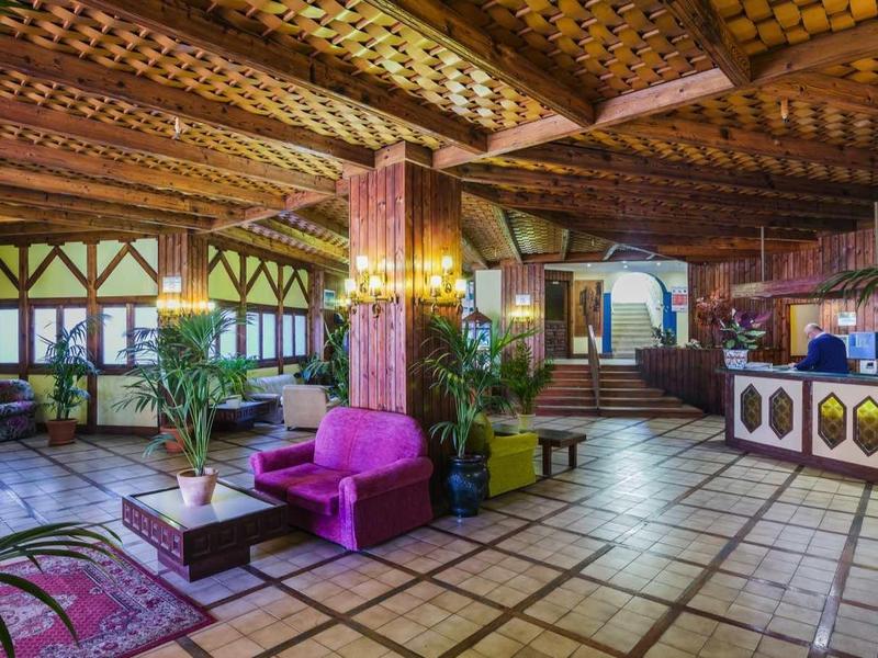 Przestronny, dekoracyjny hol hotelowy z drewnianym sufitem, roślinami i różowymi siedzeniami.