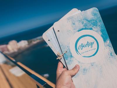 Main tenant un menu à plusieurs pages avec un design bleu et blanc sur un balcon avec vue sur la mer.