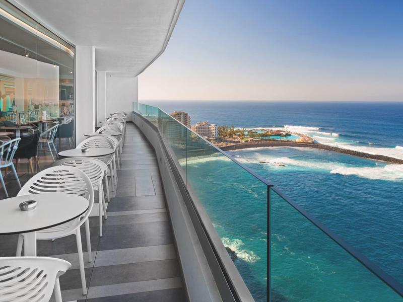 Balcon avec chaises et tables blanches donnant sur la mer et la plage