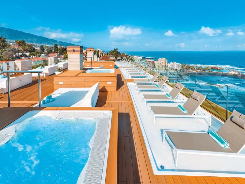 Terrasse sur le toit avec jacuzzi, chaises longues et vue sur la mer par temps ensoleillé.