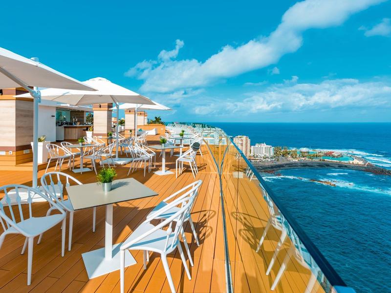 Terrasse sur le toit avec tables et chaises, vue sur l'océan et ciel bleu