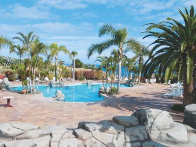 Hotelpool mit Palmen und Liegen unter blauem Himmel