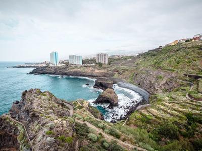 Paesaggio costiero con rocce, onde e edifici sullo sfondo sotto un cielo nuvoloso