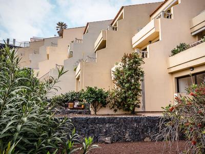 Edificio alberghiero su più piani con balconi e vegetazione lussureggiante in primo piano.