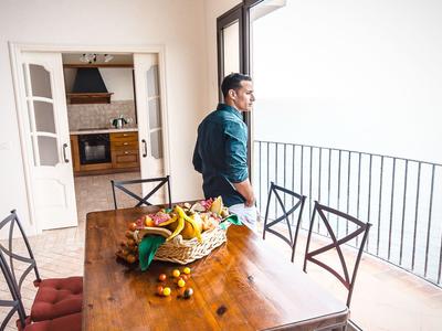 Un uomo è su un balcone e guarda fuori, accanto a un tavolo di legno con frutta.